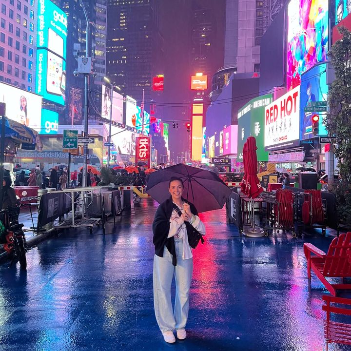 Phoebe holding an umbrella in a rainy, neon-lit Times Square