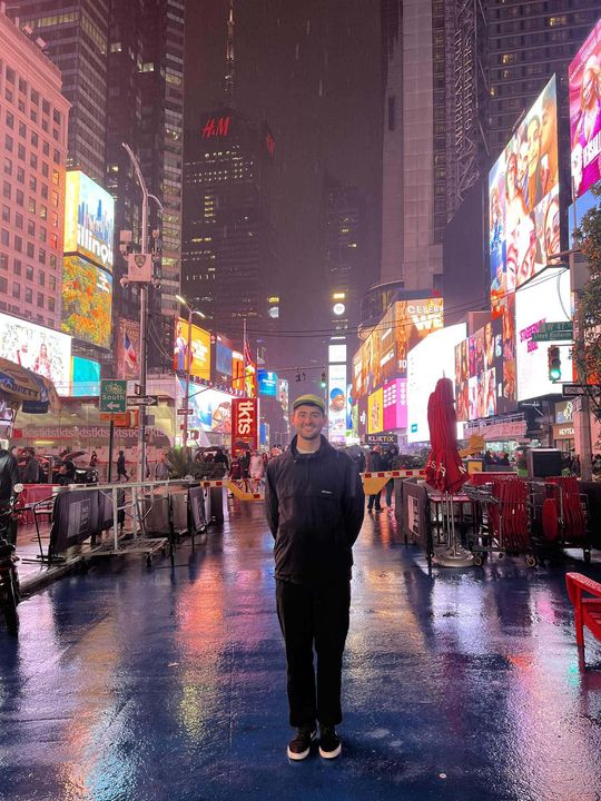Hayden standing in a rainy, neon-lit Times Square