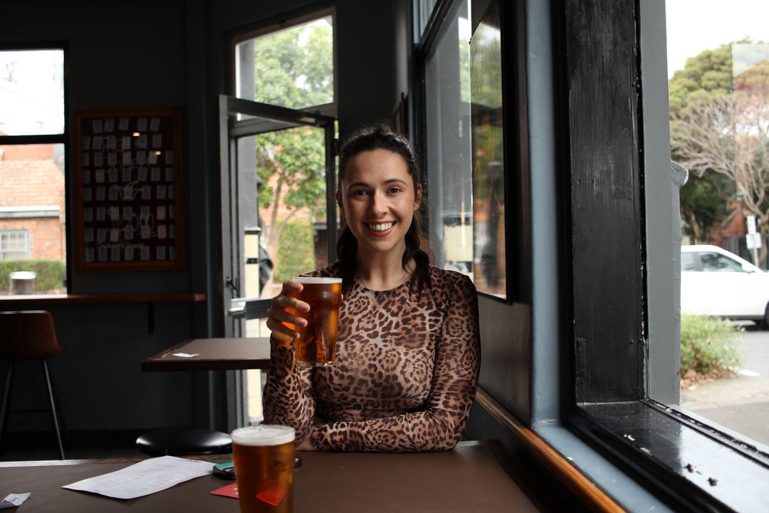 Phoebe smiling in a leopard-print top, holding a beer inside a pub