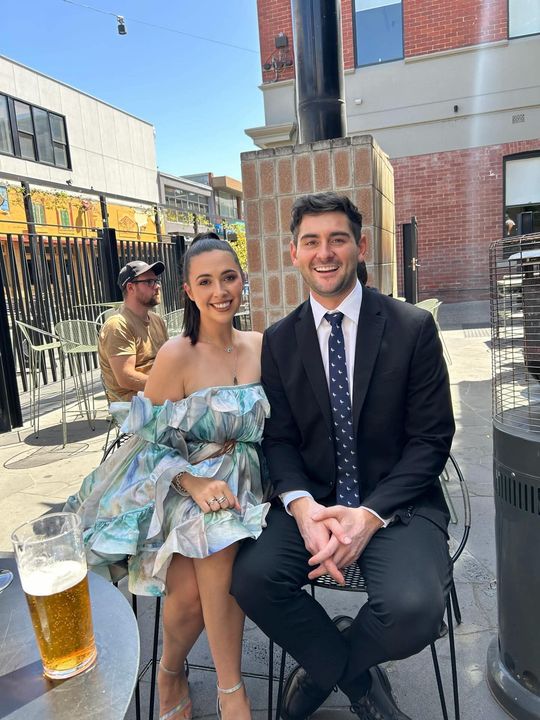 Phoebe and Hayden dressed up, having a drink in the sun